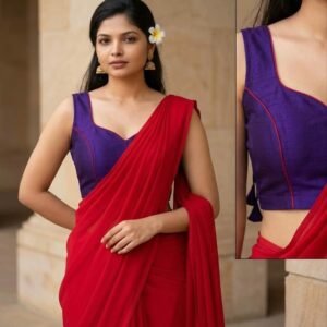 A vibrant, solid red modern-traditional fusion saree paired with a custom-tailored, sleeveless royal blue princess-cut blouse. The blouse features an elegant sweetheart neckline finished with red piping trim along the edges. Available as a new set complete with custom-tailored fitting options.